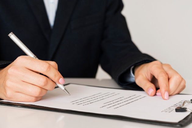 Persona sosteniendo un portapapeles y llenando un formulario con un bolígrafo, destacando el proceso de documentación y registro