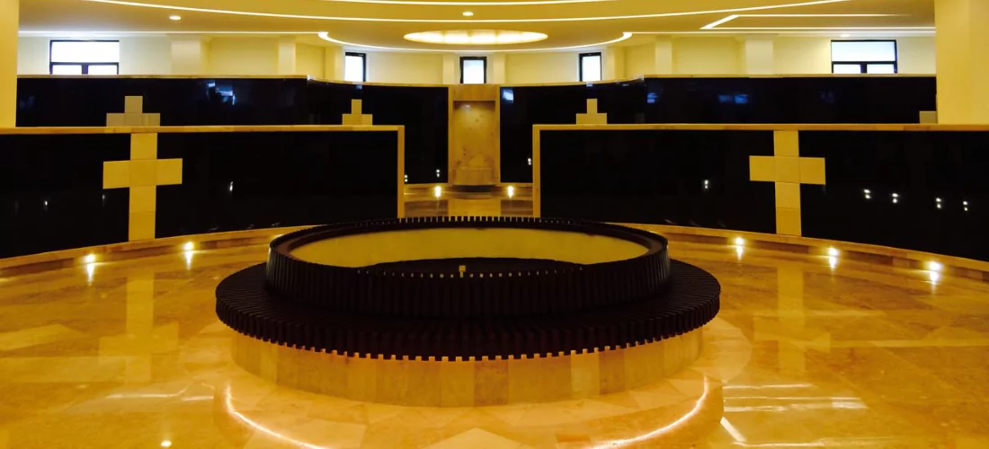 Espacio amplio con detalles en mármol beige y negro, marcado por cruces estilizadas y una fuente central en tonos oscuros