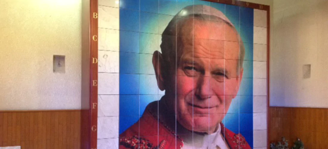 Criptas Muro de nichos con retrato de San Juan Pablo II sobre fondo azul, enmarcado en mármol blanco y detalles en rojo, brindando un ambiente de respeto y devoción