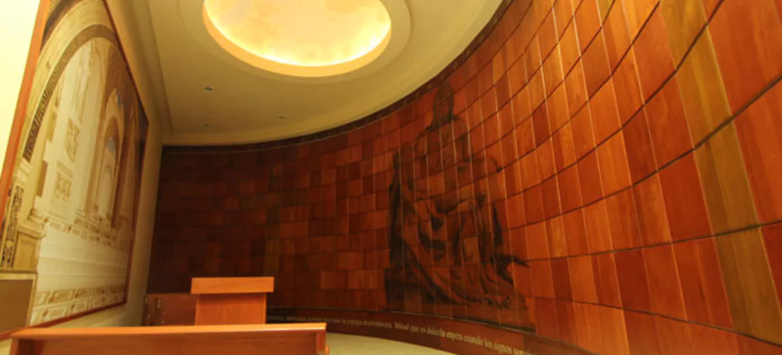 Criptas Espacio curvo con nichos en tonos cálidos de madera, decorado con la imagen de La Piedad y una cúpula iluminada que proporciona un ambiente de paz y serenidad.
