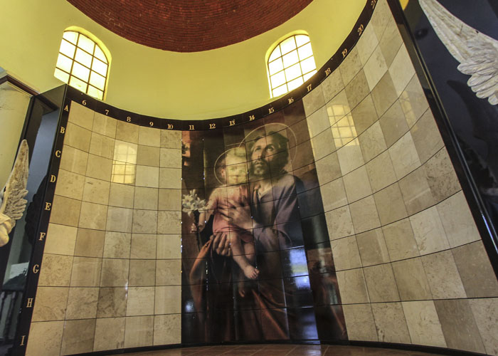 Criptas Pared curva con azulejos claros y una imagen religiosa central, iluminada por ventanales superiores