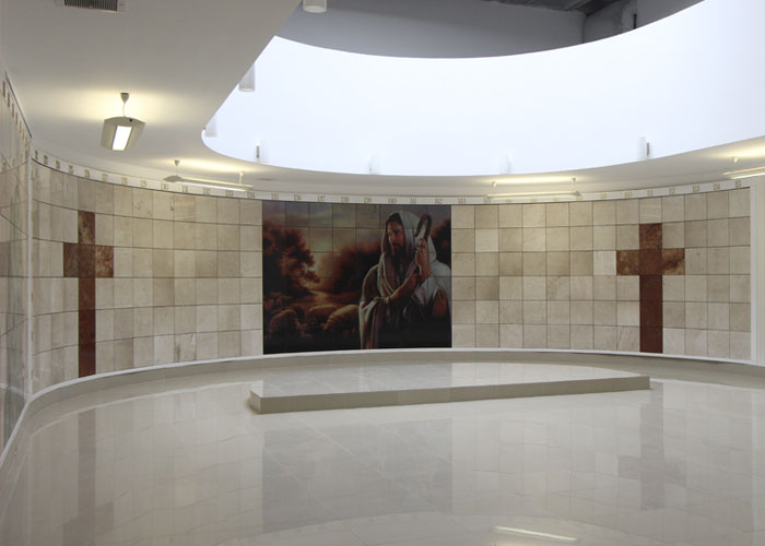 Criptas Sala circular con un mural central de Jesús y cruces de mármol en los lados.