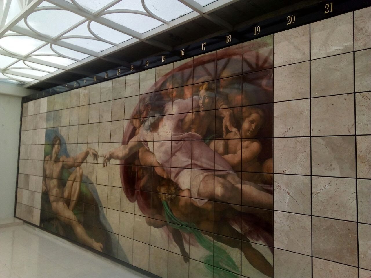 Criptas Mural de nichos con la recreación de la obra "La Creación de Adán" de Miguel Ángel, en un espacio con techo de diseño moderno.