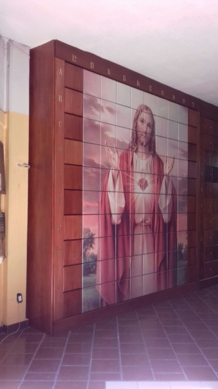 Criptas Mural de nichos con imagen de Jesús, representado con el Sagrado Corazón sobre un fondo de cielo al atardecer, enmarcado en estructura de madera.