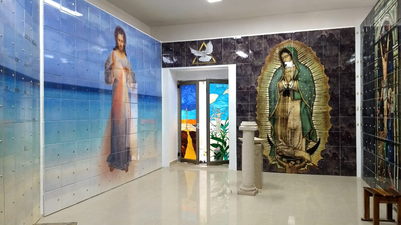 Criptas Espacio interior con murales religiosos de Jesús y la Virgen de Guadalupe en mosaico, acompañado de una puerta con vitrales coloridos