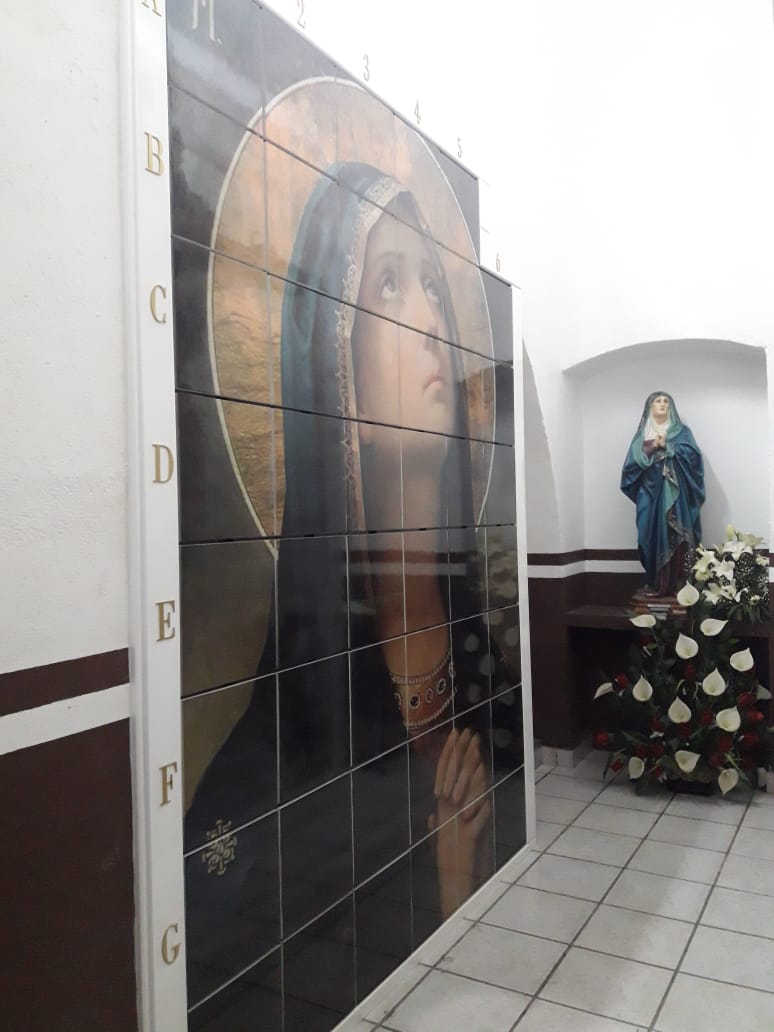 Criptas Mural en mosaico de la Virgen María, con numeración en los bordes, junto a una estatua de la Virgen y flores