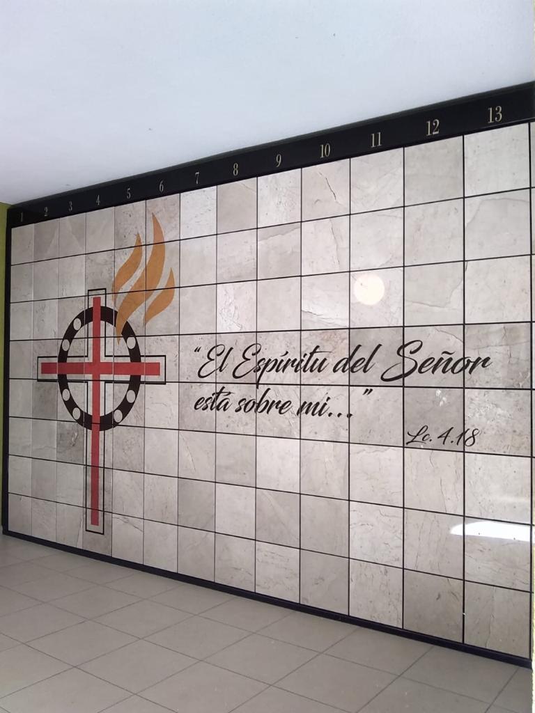 Criptas Pared con mosaico que muestra una cruz con flamas y la frase 'El Espíritu del Señor está sobre mí...' (Lc 4,18), con numeración en la parte superior